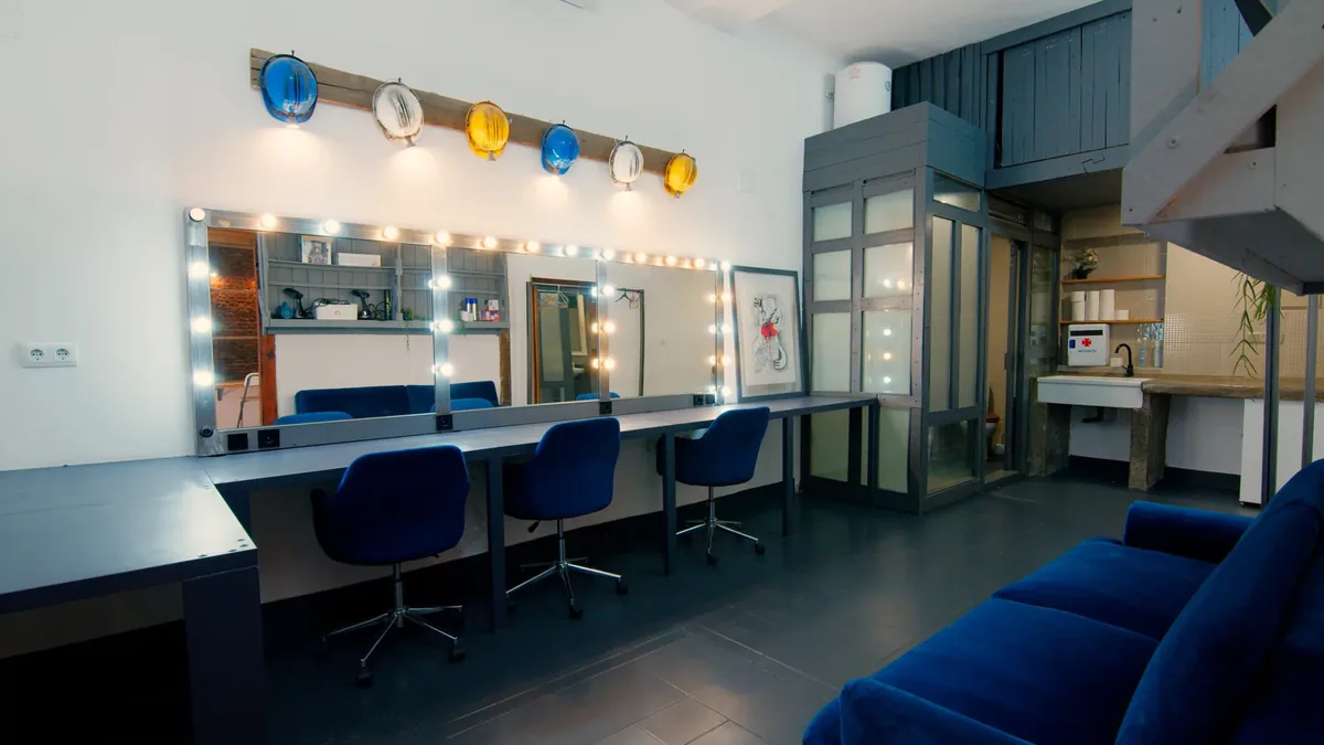 Dressing room at Plató La Mina with a lit mirror vanity, three make-up chairs and a lounge sofa